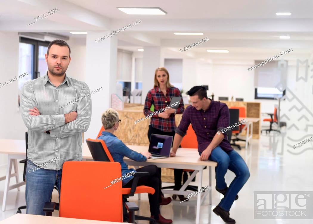 Imagen: portrait of young businessman in casual clothes at modern startup business office space, team of people working together in background.