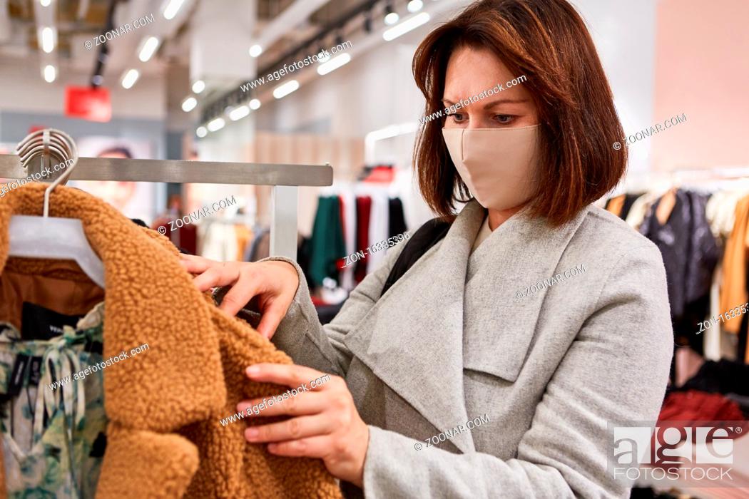 Stock Photo: Frau als Kundin mit Gesichtsmaske wegen Covid-19 Pandemie in einer Mode Boutique.