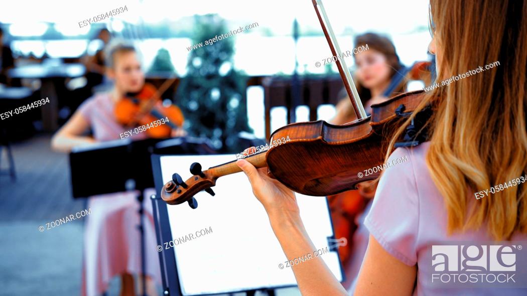 Stock Photo: Little Group Of Violins In Pink Concert Dresses Plays Together On A Sunny Terrace. Focus On The Girl On The Right Back View.