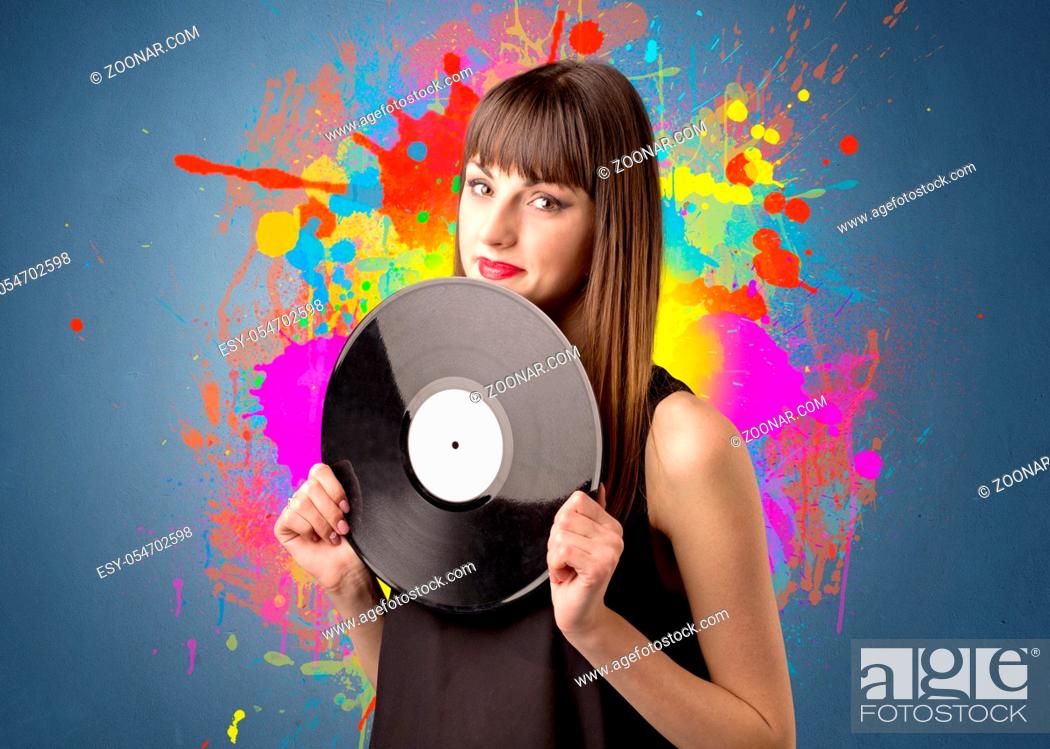 Stock Photo: Young lady holding vinyl record on a grey background with colorful splashes behind her.