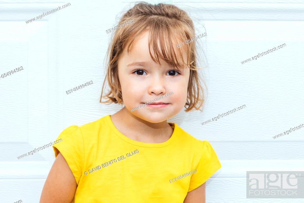 Stock Photo: Adorable blond-haired girl wearing a yellow shirt leaning against white background.
