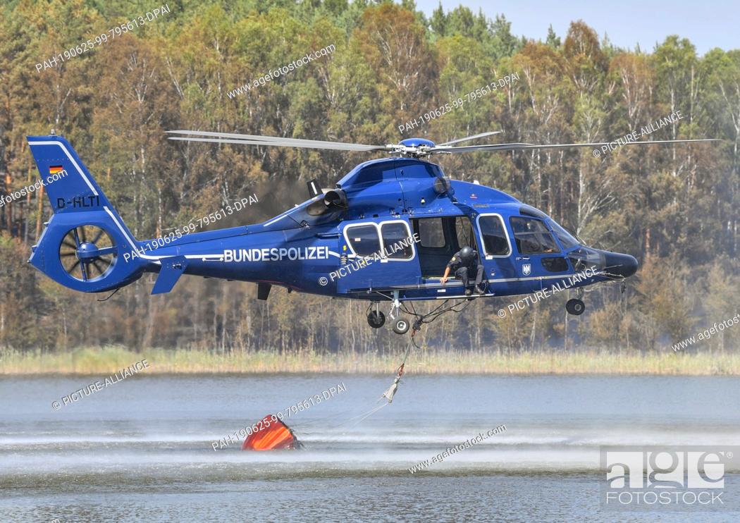 Stock Photo: 25 June 2019, Brandenburg, Lieberose: A helicopter of the federal police picks up water in the tar furnace lake to fight the forest fire in the Lieberoser Heide.