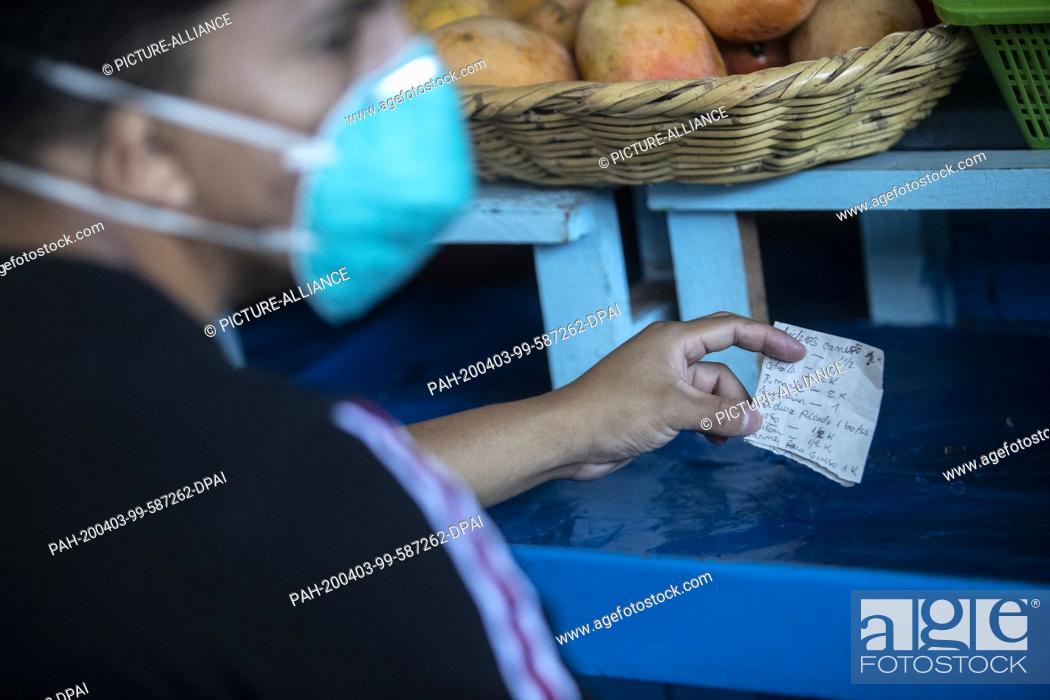 Stock Photo: 03 April 2020, Peru, Lima: A man wearing a face mask against the spread of the coronavirus holds a shopping list in front of a market stall.