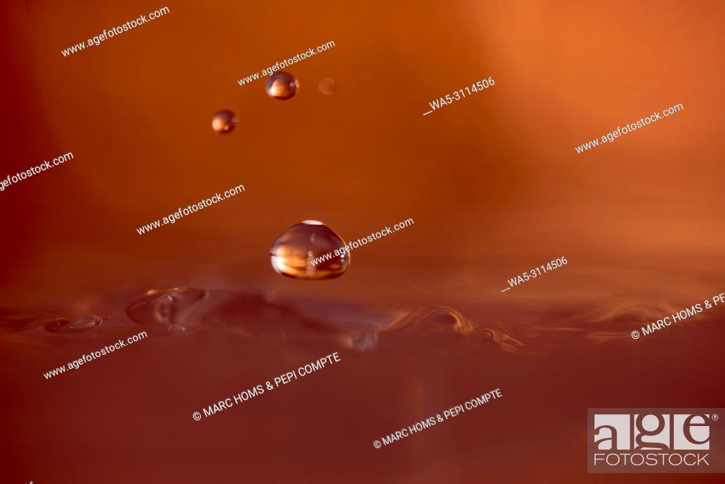 Stock Photo: Three drops of copper-colored water suspended above the surface of the water.