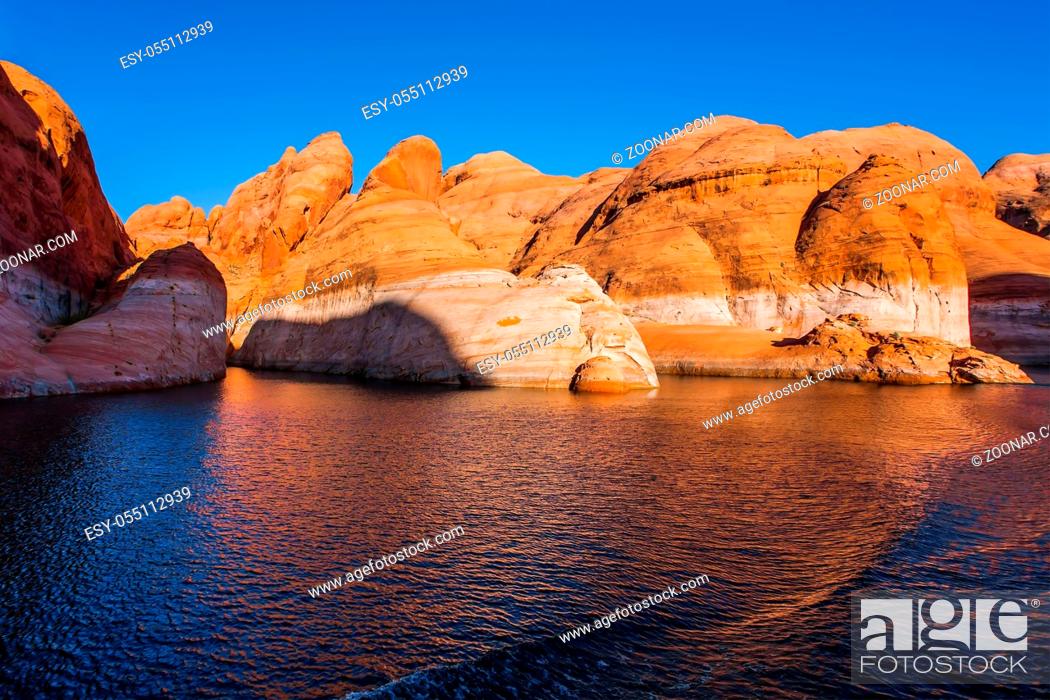Stock Photo: Sunset. Grandiose cliffs - red sandstone outcroppings. Tour on a tourist boat on an artificial reservoir Lake Powell. The Colorado River and Antelope Canyon.