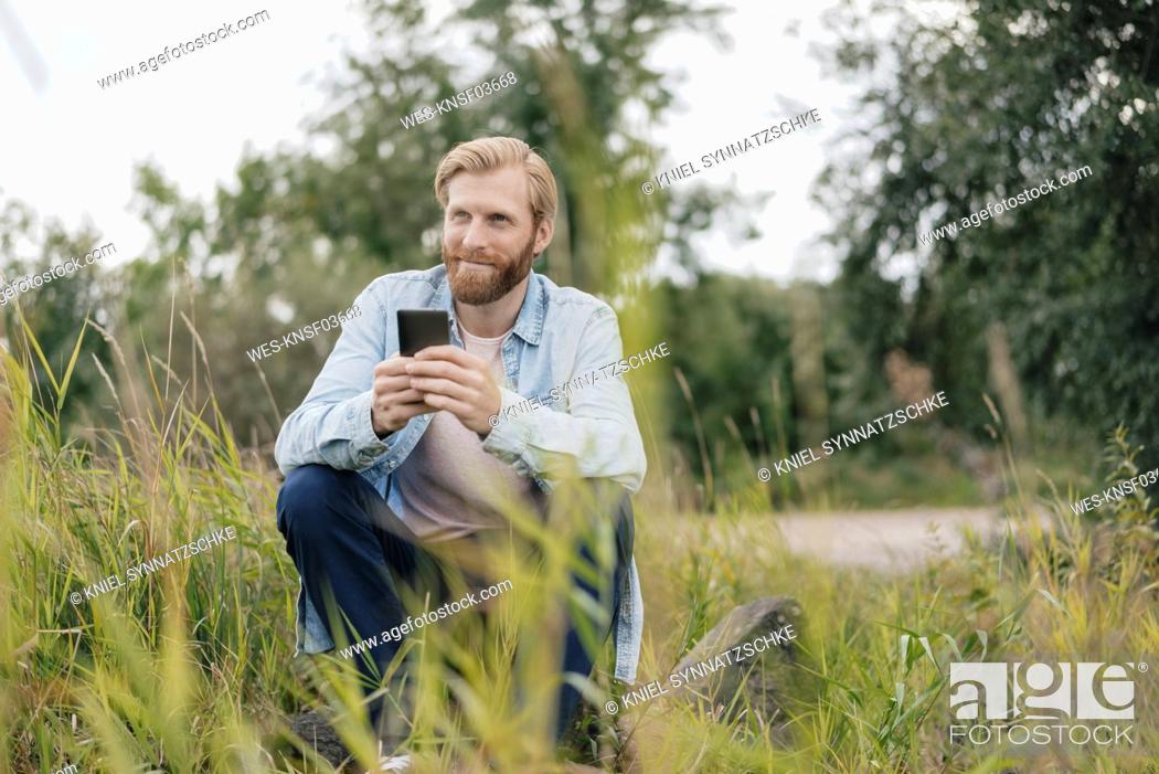 Stock Photo: Smiling man using smartphone in nature.