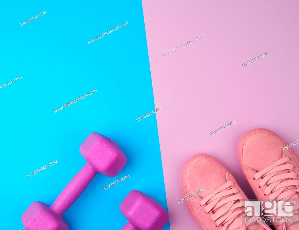 Photo de stock: pair of pink leather sneakers, plastic dumbbells for sports on a pink blue background, sports backdrop, top view, copy space.