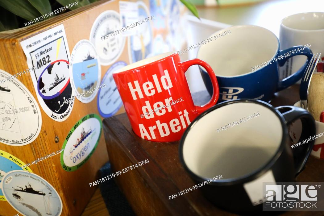 Stock Photo: 19 December 2018, Hamburg: Coffee cups, one with the inscription ""Held der Arbeit"", are standing in a holder on the bridge of the research vessel ""Meteor"".