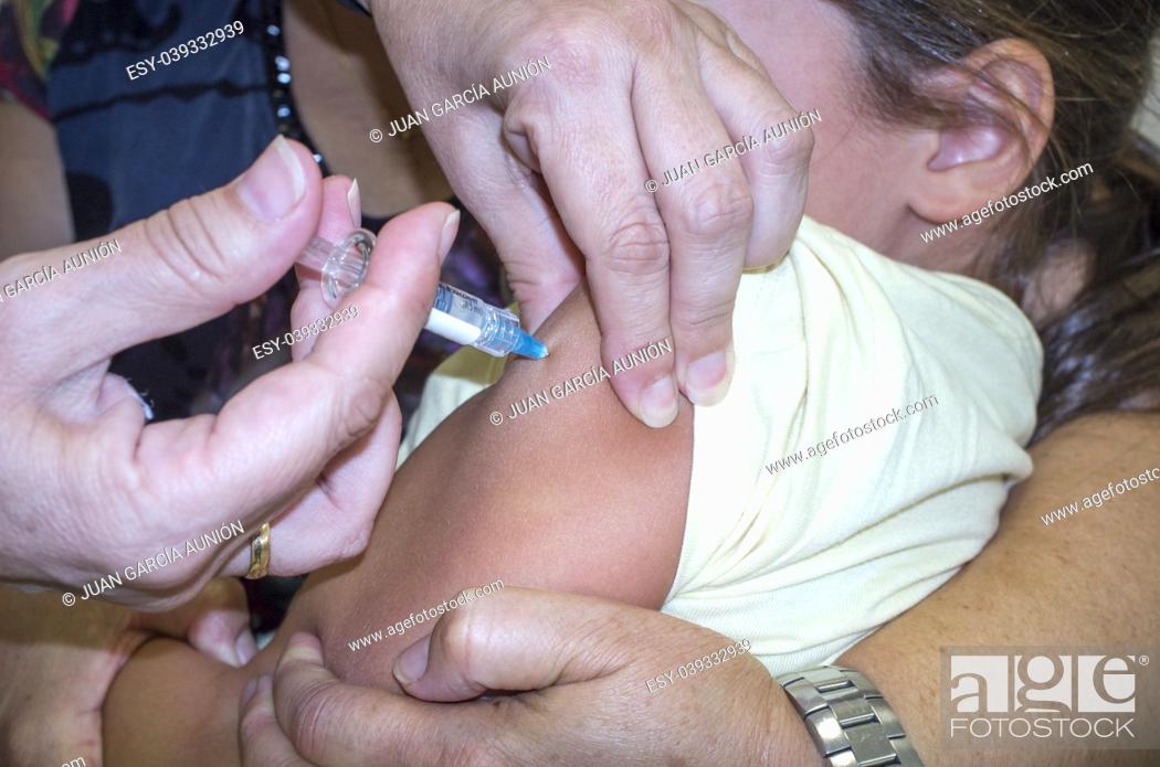 Stock Photo: Mature nurse vaccinating a little girl while the mother is hugging her. She is stabbing the needle.