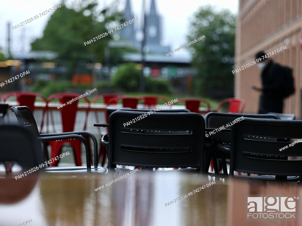 Stock Photo: 26 May 2021, North Rhine-Westphalia, Cologne: Chairs and tables stand outside a restaurant in the rain, with the cathedral in the background.