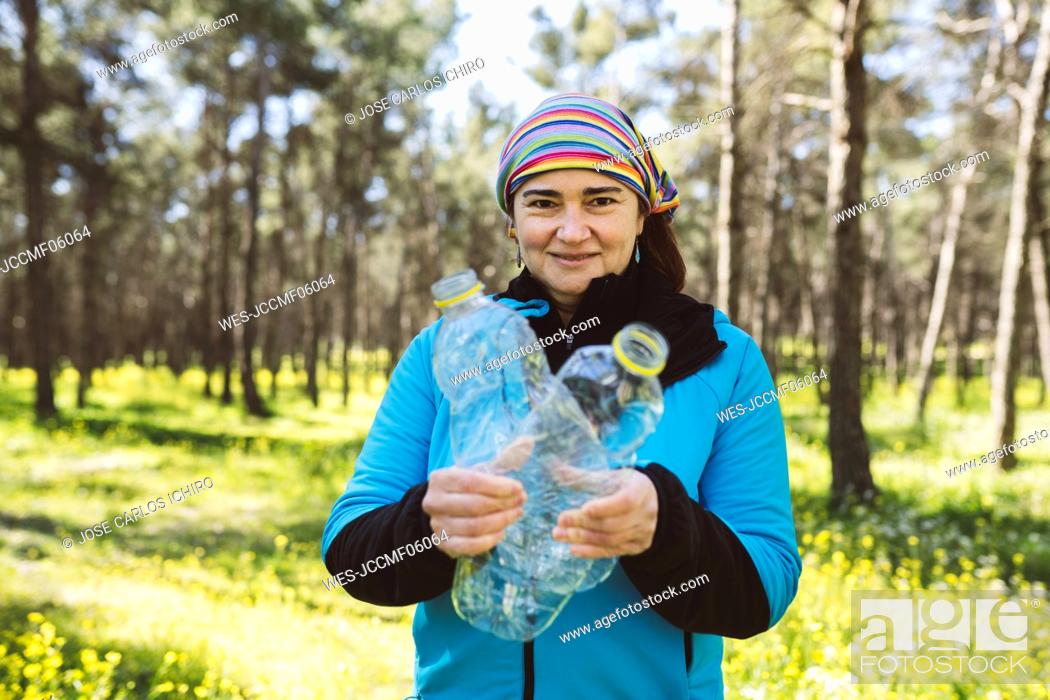 Stock Photo: Smiling woman with plastic bottles standing in forest.
