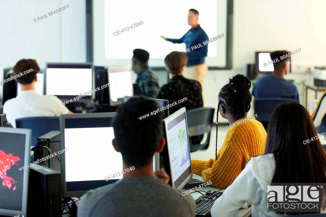 Stock Photo: Junior high students at computers watching teacher at projection screen in classroom.