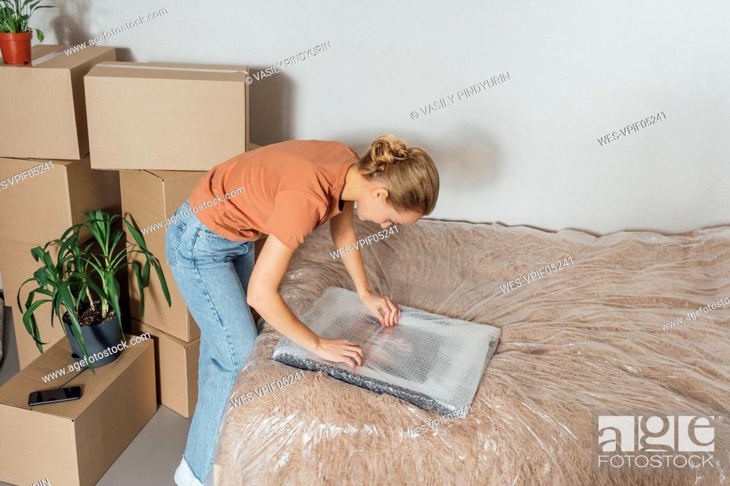 Stock Photo: Woman unwrapping picture frame in relocated apartment.