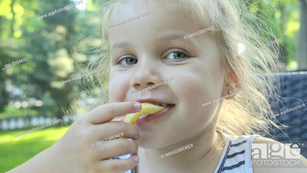 Stock Photo: Little girl eat french fries. Close-up of blonde girl takes potato chips with her hands and tries them sitting in street cafe on the park.