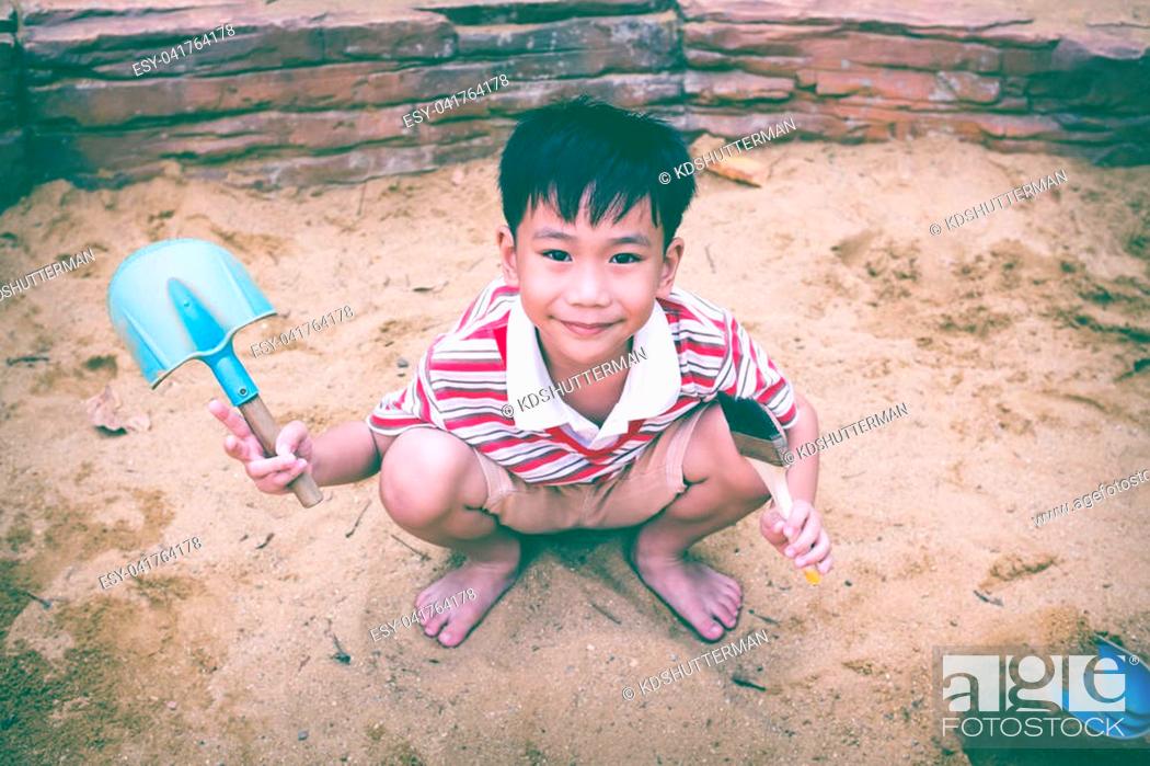 Stock Photo: Happy child playing with sand and smiling. Adorable asian boy has fun digging in the sand on a summer day and looking at camera. Vintage tone.