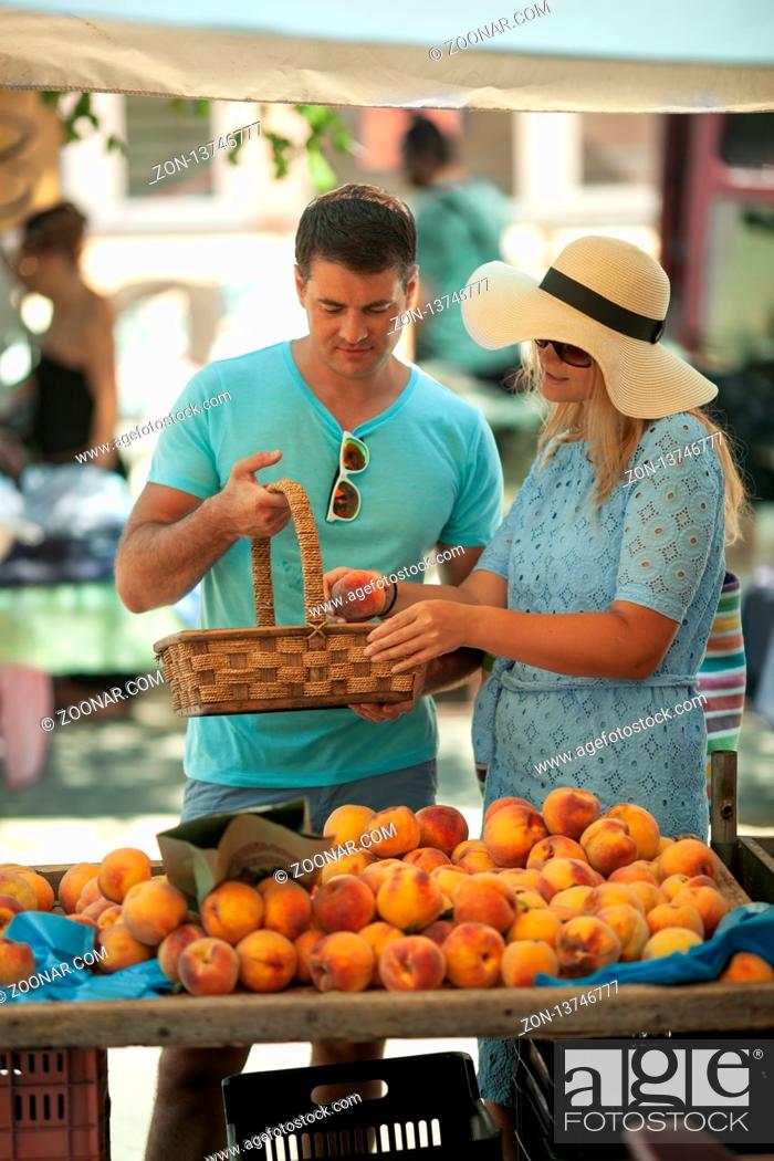 Stock Photo: A young couple with a basket chooses peaches at the counter.