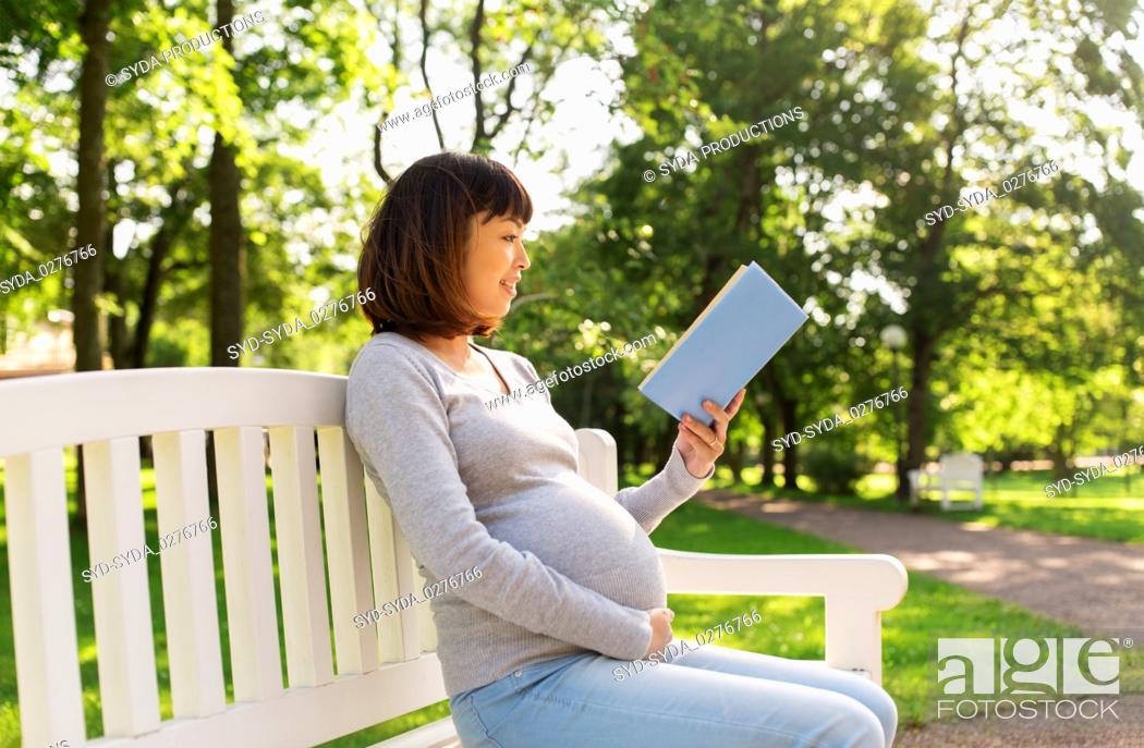 Stock Photo: happy pregnant asian woman reading book at park.