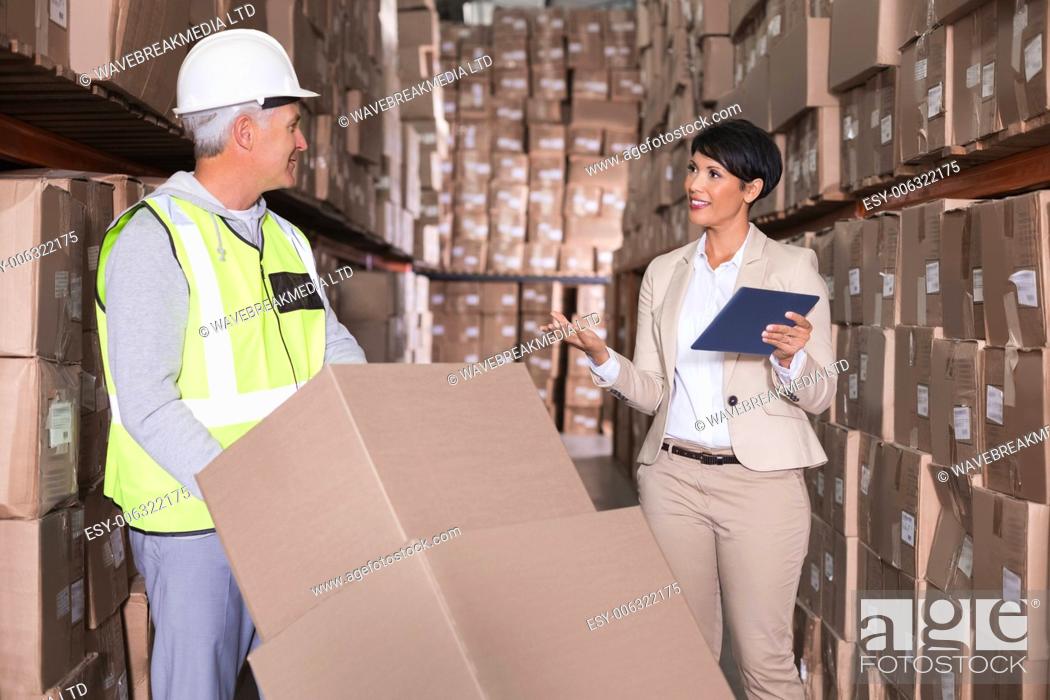 Stock Photo: Warehouse worker moving boxes on trolley talking to manager in a large warehouse.