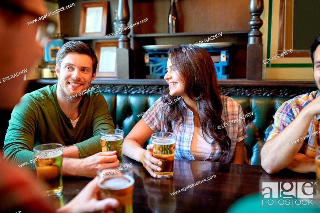 Imagen: people, leisure, friendship and communication concept - happy friends drinking beer and talking at bar or pub.
