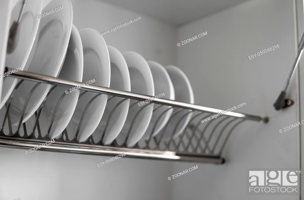 Imagen: Dish drying metal rack with big nice white clean plates. Traditional comfortable kitchen. Open white dish draining closet with wet dishes of glass and ceramic.
