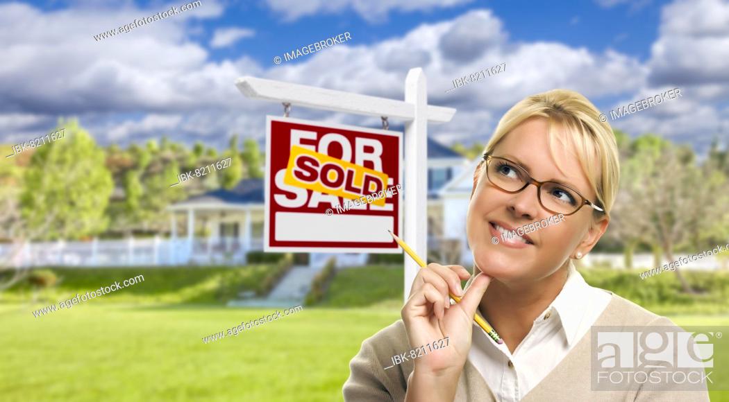 Stock Photo: Attractive young adult woman with pencil in front of sold for sale real estate sign and house.
