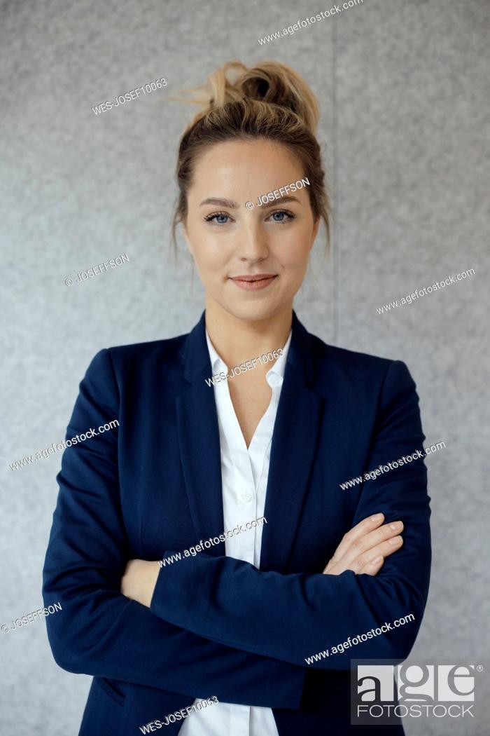 Stock Photo: Businesswoman with arms crossed in front of gray wall.