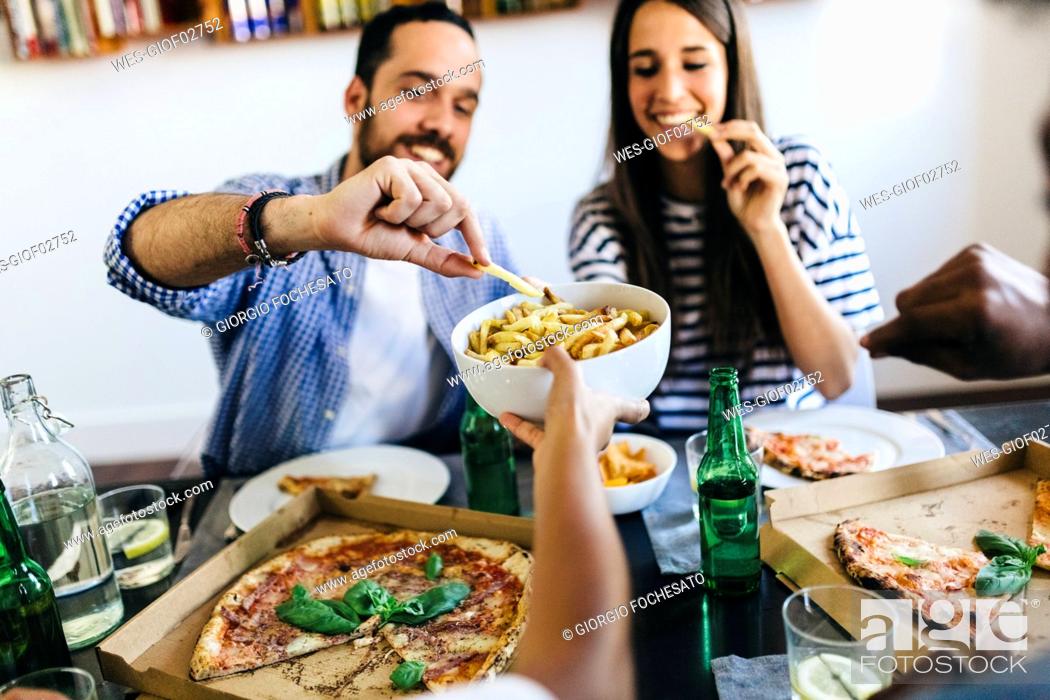 Stock Photo: Happy friends having French fries and pizza at home.