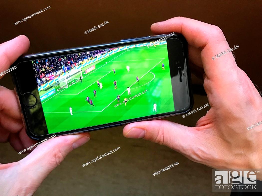 Stock Photo: Hands holding a smartphone showing a football match.