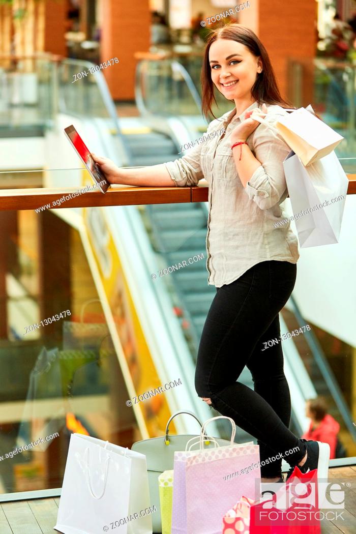 Stock Photo: Glückliches Mädchen im Shoppingcenter mit Tablet PC und vielen Einkaufstüten.