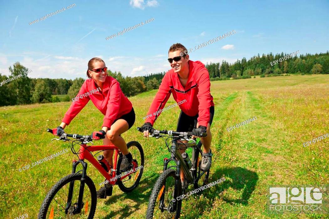 Photo de stock: Young couple riding mountain bike in spring meadow.