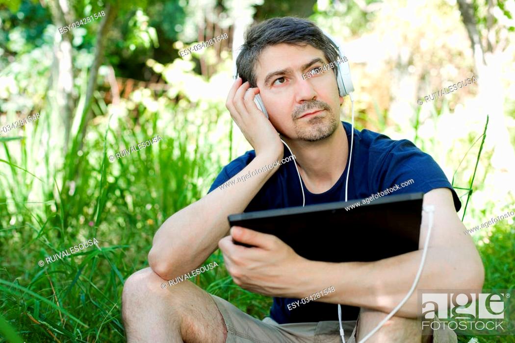 Stock Photo: young man holding a tablet with headphones, outdoor.