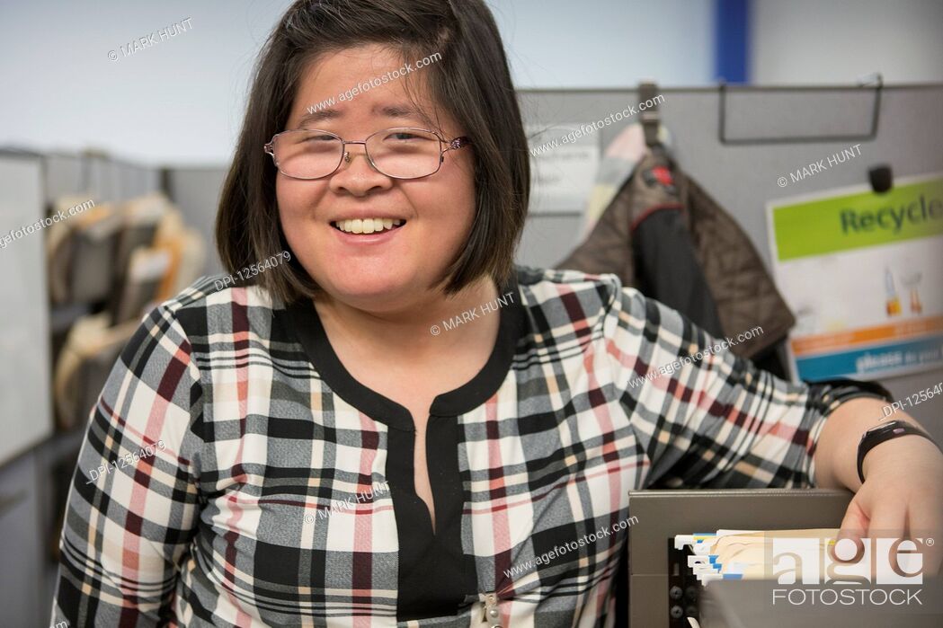 Stock Photo: Asian woman with a Learning Disability using a file cabinet in office.
