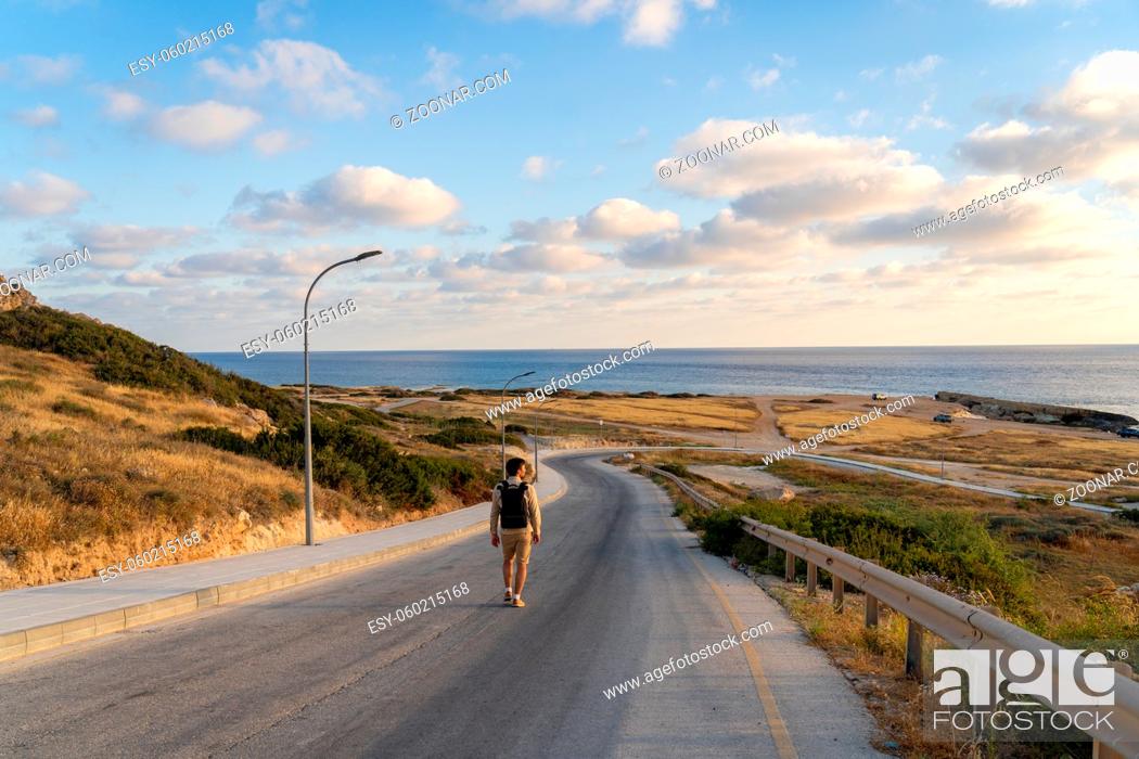 Stock Photo: Backpacker hikes on the island of Cyprus, man with backpack walks along the highway on hill near Mediterranean Sea in Agios Georgios Pegeias.
