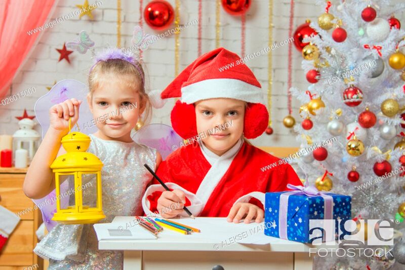 Stock Photo: A girl dressed in a red suit Santa Claus draws pencils sitting at the table, next is a girl dressed as a fairy with the candlestick.