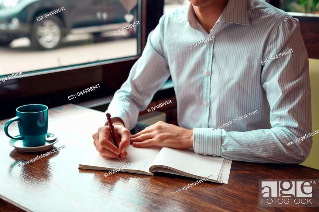 Stock Photo: Full concentration man with coffee. Close-up part of young businessman writing in notebook while sitting at his working place outdoor.