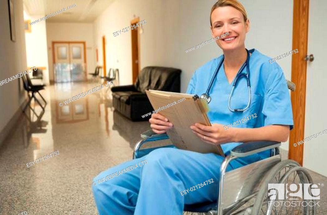 Stock Photo: Smiling nurse in a wheelchair holding a folder in hospital corridor.
