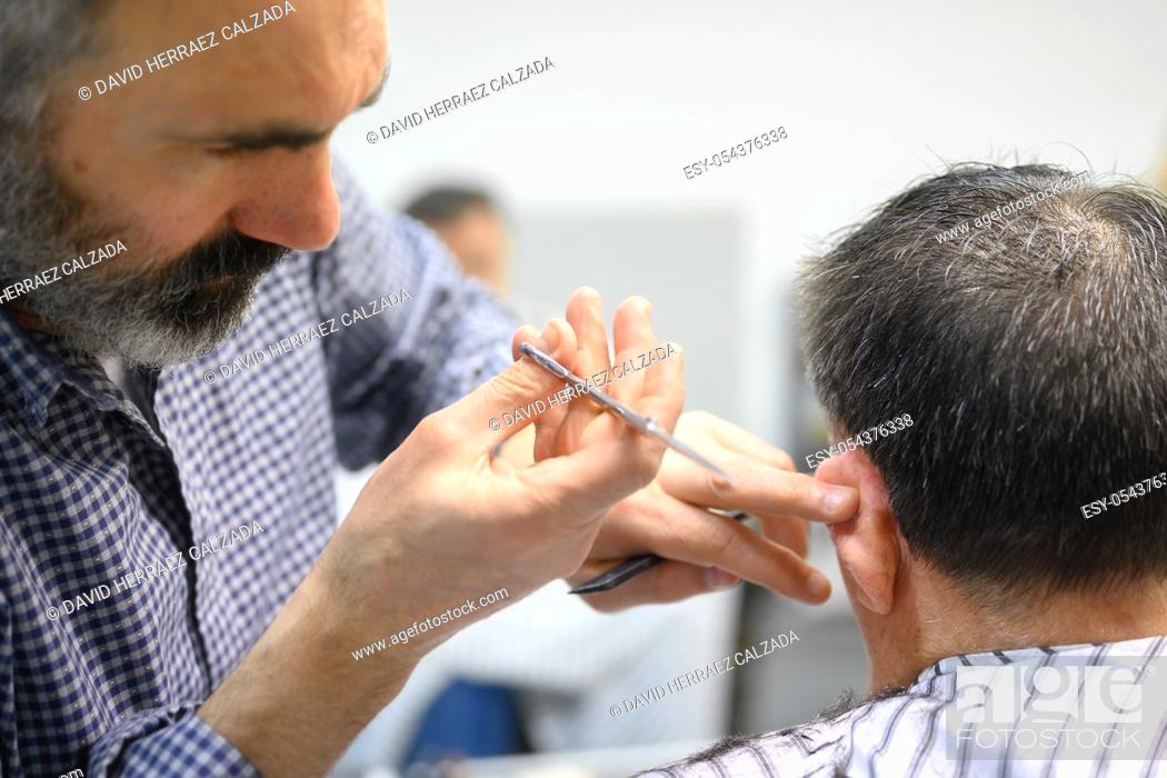 Stock Photo: Barber trimming hair of old man at barber shop .