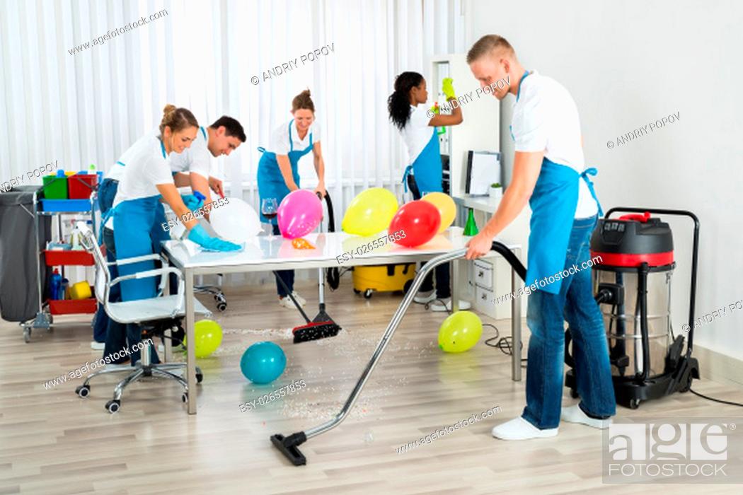 Stock Photo: Group Of Male And Female Janitors Cleaning The Office After Party.