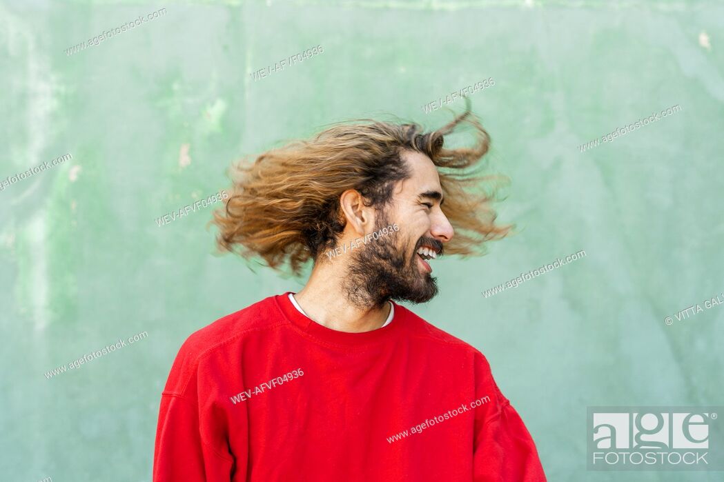 Stock Photo: Bearded young man with tossing his hair in front of green wall.