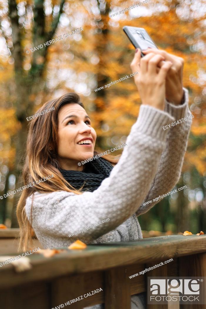 Stock Photo: Beautiful young happy woman taking selfie with smartphone in autumn park. Season, technology and people concept .