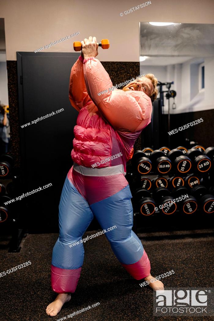 Stock Photo: Man in gym wearing pink bodybuilder costume lifting dumbbell.