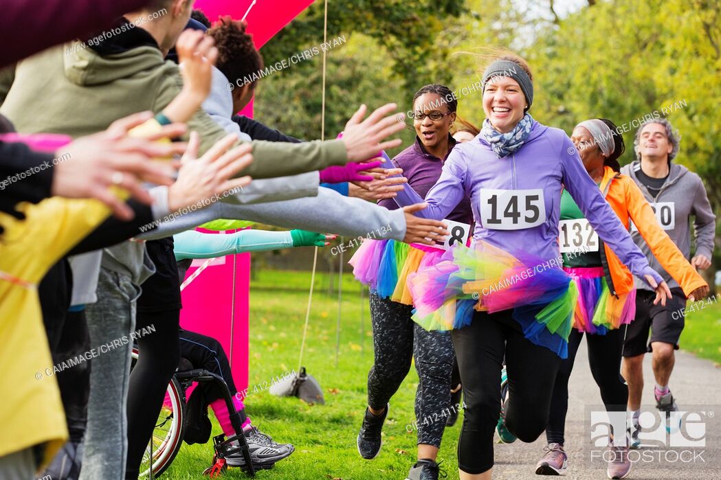 Photo de stock: Enthusiastic female runners in tutus high-fiving spectators at charity run in park.