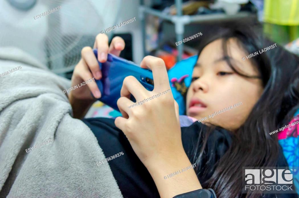 Stock Photo: An Asian girl is addicted to a cell phone game lying on a bed.Focus on the hand.