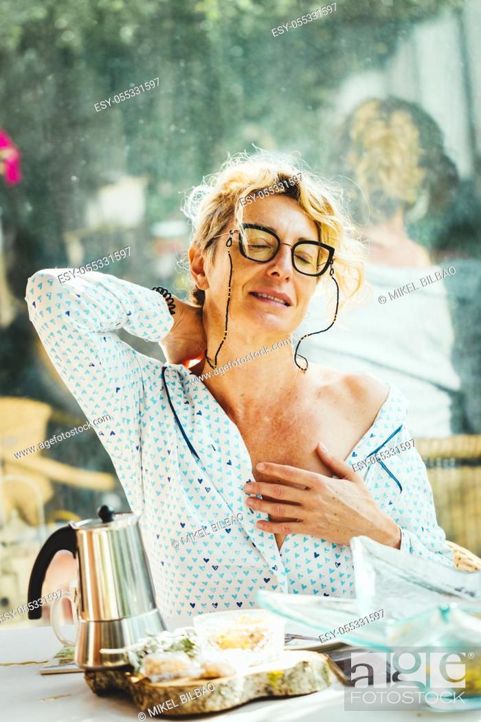 Stock Photo: Blonde young mature woman with glasses in pyjamas at home in breakfast time, with backache.