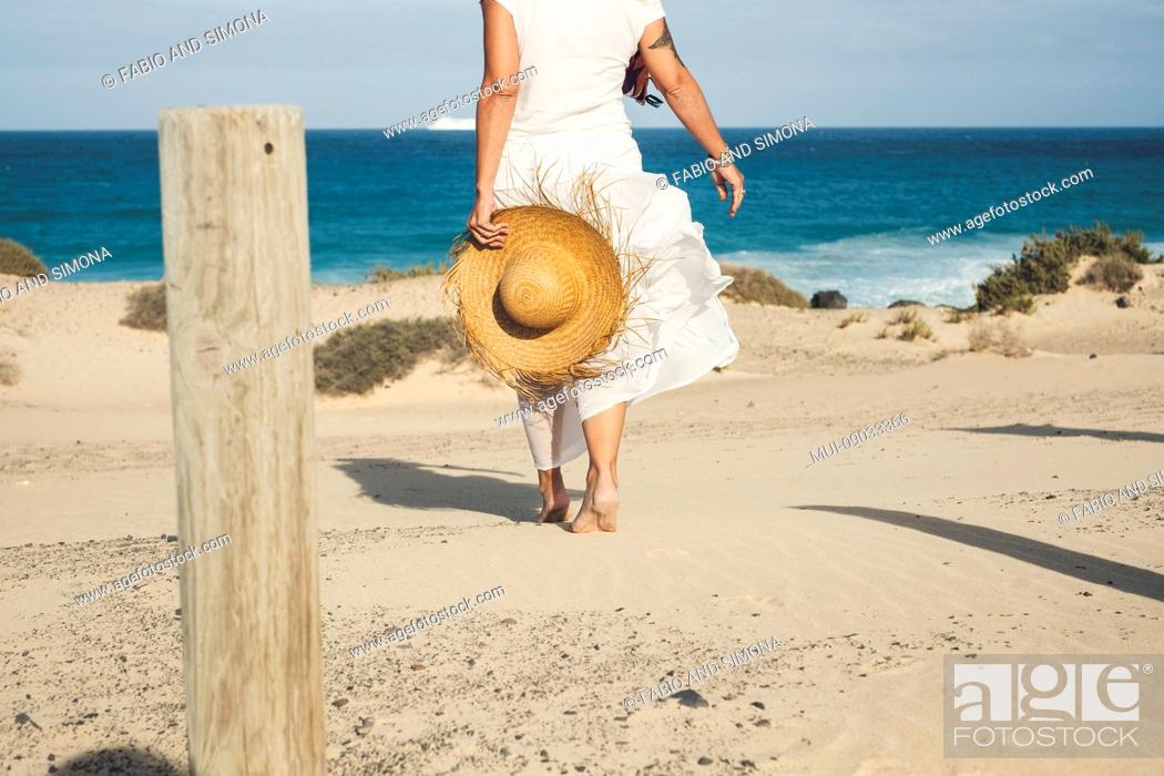 Stock Photo: Elegant fashion lady in white dress and natural hat walking to the beach barefoot enjoying the summer holiday vacation day in tropical place - blue sea and sky.
