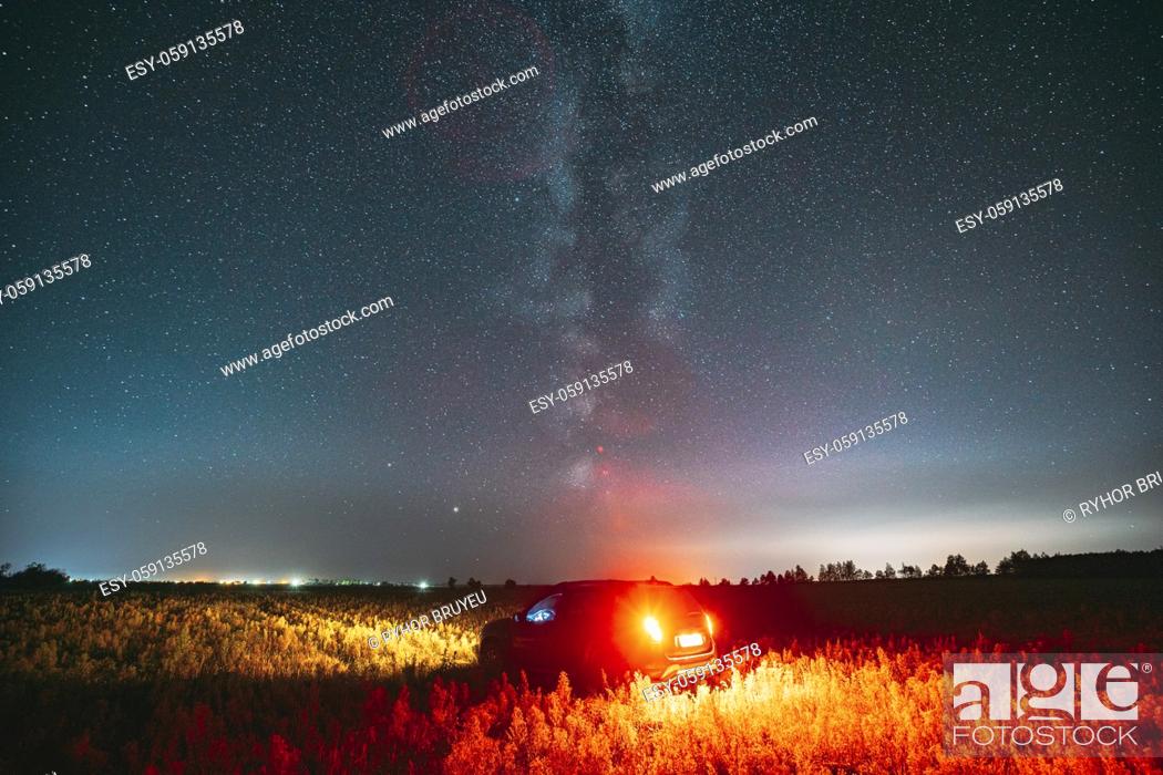 Stock Photo: Milky Way Galaxy In Night Starry Sky With Glowing Stars Above Car SUV In Countryside Landscape. Milky Way Galaxy And Rural Field Meadow.