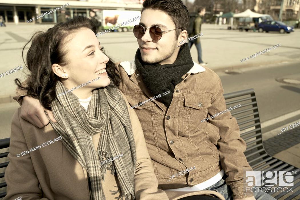 Stock Photo: young teenage couple sitting together on bench in city, looking at each other, in Cottbus, Brandenburg, Germany.