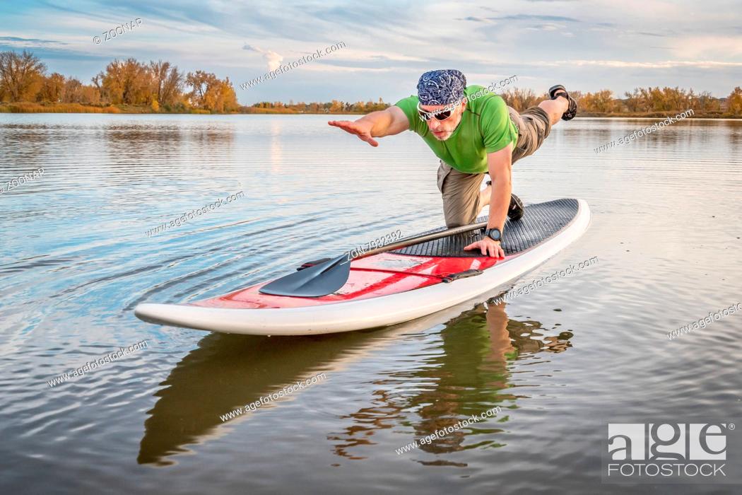 Stock Photo: senior male stretching and warming up on a paddleboard before paddling workout on a lake in Colorado.