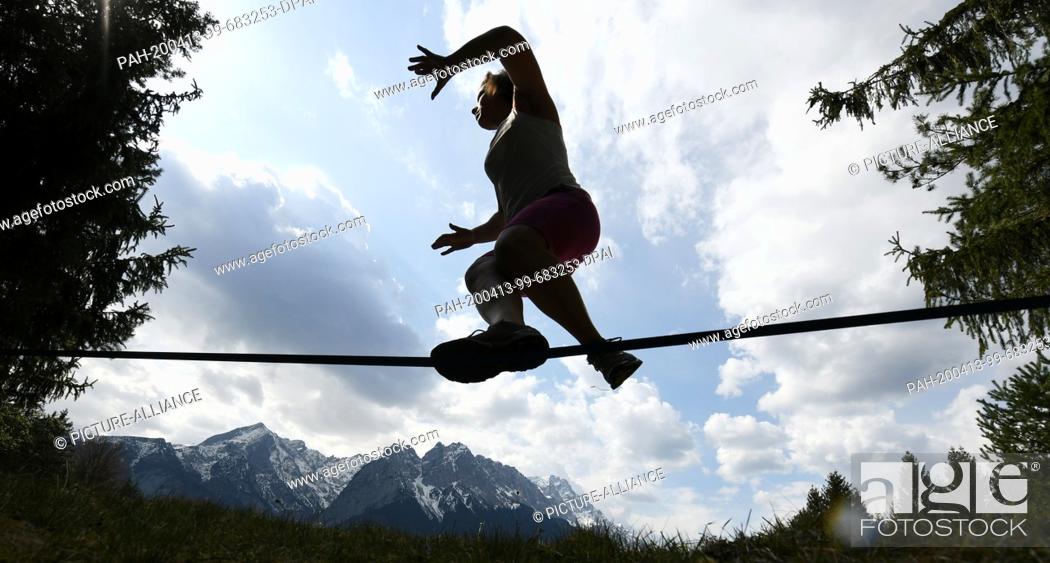 Stock Photo: 13 April 2020, Bavaria, Garmisch-Partenkirchen: A young woman is balancing on a slackline, the Wettersteingebirge can be seen in the background.