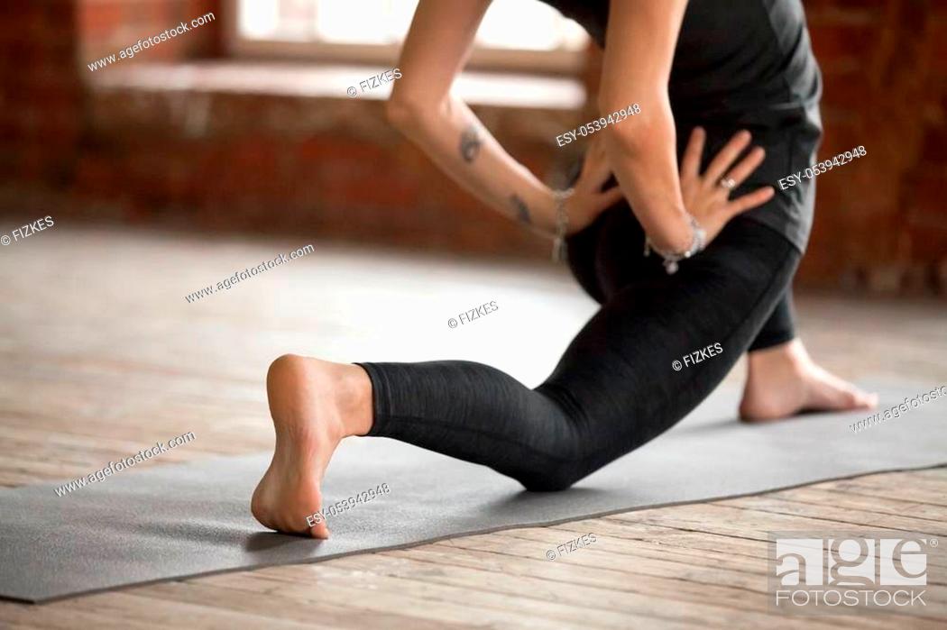 Stock Photo: Young woman practicing yoga, doing Horse rider exercise, anjaneyasana pose, working out, wearing sportswear, black pants and top, indoor close up.